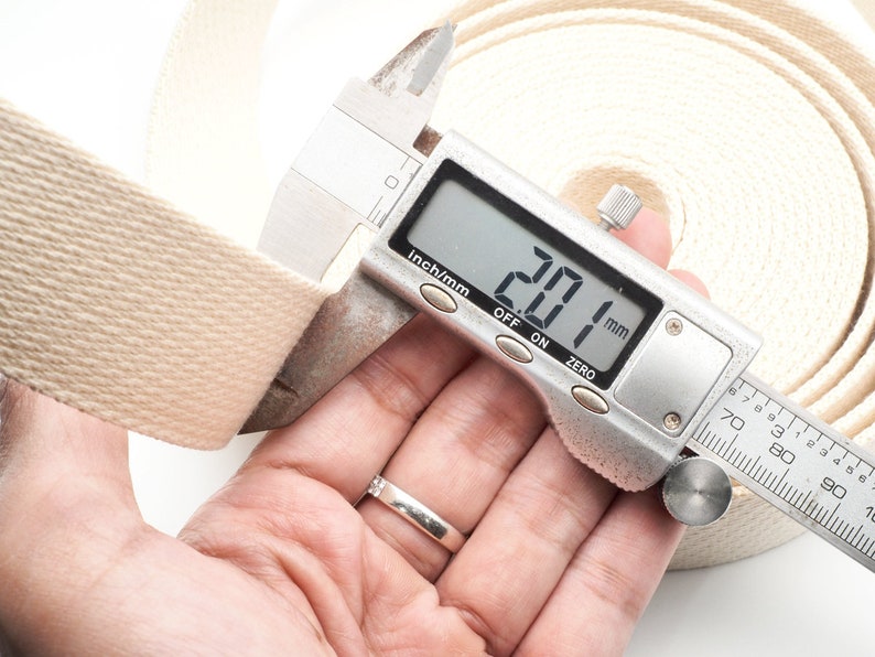 May include: Close-up of a beige cotton webbing roll being measured with a digital caliper. The caliper reads 20.1 mm.