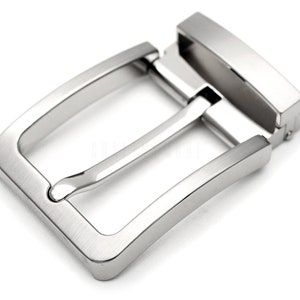 May include: A silver metal belt buckle with a smooth, brushed finish. The buckle has a rectangular shape with rounded corners and a single prong.
