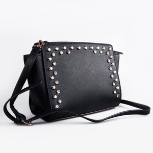 May include: Black leather shoulder bag with a silver studded trim around the flap. The bag has a long adjustable strap.