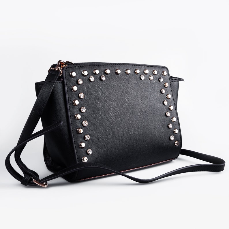 May include: Black leather shoulder bag with a silver studded trim around the flap. The bag has a long adjustable strap.