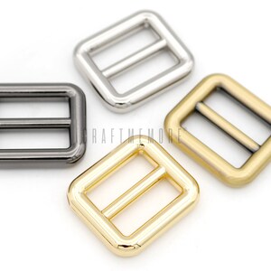 May include: Three metal slider buckles in different finishes: silver, black, and gold. Each buckle is square-shaped with a rectangular opening and a bar across the middle.