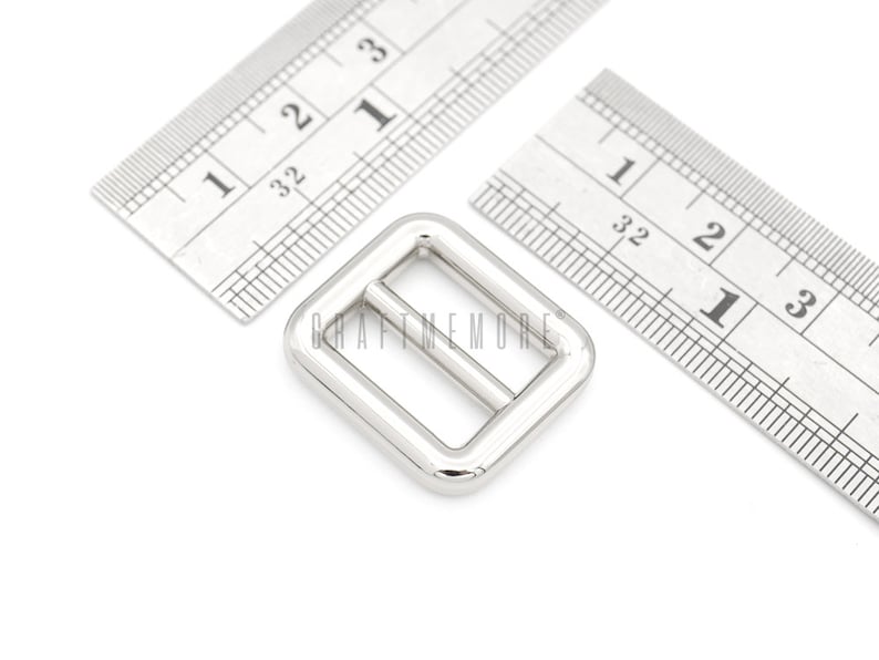 May include: Silver metal buckle measuring 1 inch by 1 inch. The buckle is rectangular with a smooth, polished finish.