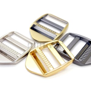 Puede incluir: Cuatro hebillas deslizantes de metal en diferentes acabados: plata, oro, negro y bronce. Las hebillas son rectangulares con esquinas redondeadas y tienen dos ranuras paralelas para una correa.