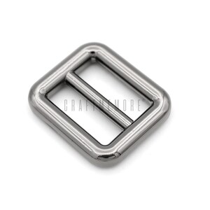 May include: Silver metal buckle with a rectangular shape and a smooth finish. The buckle has two slots for a strap or ribbon.