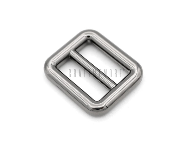 May include: Silver metal buckle with a rectangular shape and a smooth finish. The buckle has two slots for a strap or ribbon.