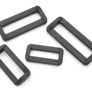 May include: Four black plastic slider buckles of different sizes. The buckles are rectangular with a slot in the middle.