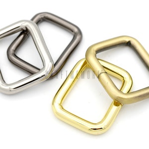 Op de afbeelding: Drie metalen D-ringen in zilver, goud en gunmetal afwerking. De ringen zijn vierkant met afgeronde randen.