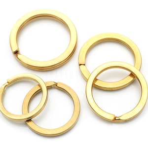 May include: Four gold-colored metal key rings of different sizes. The key rings are arranged in a cluster on a white background.