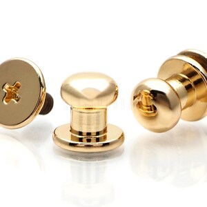 May include: Three gold-toned metal push button fasteners with a screw-on back. The fasteners have a round head and a cylindrical base.
