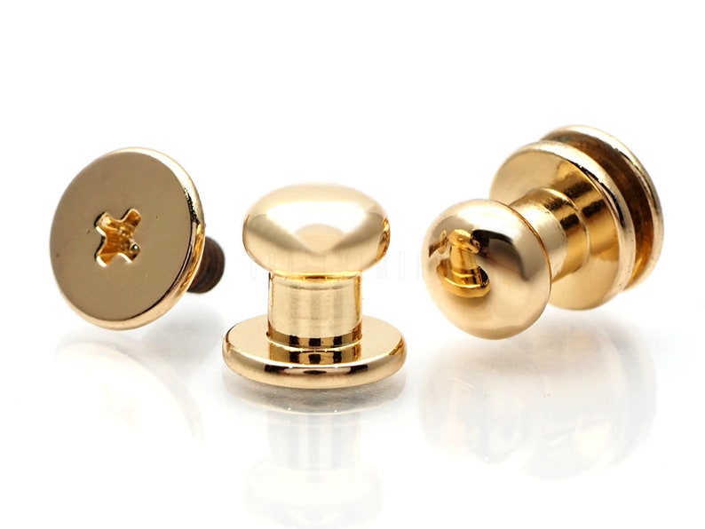 May include: Three gold-toned metal push button fasteners with a screw-on back. The fasteners have a round head and a cylindrical base.