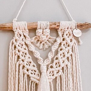 May include: A beige macrame wall hanging with a wooden dowel and a small wooden tag that says "Odds and Ends Boutique".
