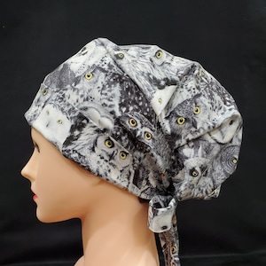 May include: A black and white patterned surgical scrub hat with a tie. The pattern features a repeating image of owls with yellow eyes.
