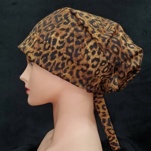 Op de afbeelding: Een bruine en zwarte chirurgische scrub-muts met een luipaardprint en een lange stropdas. De muts is gemaakt van een zachte, comfortabele stof en is perfect om haar uit het gezicht te houden tijdens een operatie of andere medische procedures.