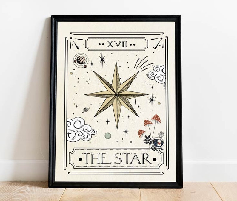 May include: A black framed print of a tarot card depicting The Star. The card features a large, eight-pointed star with a yellow centre and a white outline. The star is surrounded by clouds, stars, and mushrooms. The card is titled "The Star" and numbered "XVII".