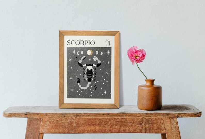 May include: A framed print with a black and white illustration of a scorpion with a crescent moon and stars on a dark gray background. The text "SCORPIO" and the astrological symbol for Scorpio are printed in the top left and right corners of the print.