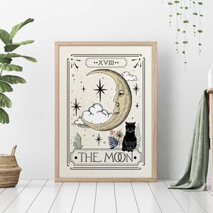 K&ouml;nnte beinhalten: Ein gerahmter Druck einer Tarotkarte, die die Mondkarte darstellt. Die Karte zeigt einen Halbmond mit einem Gesicht, eine schwarze Katze und Sterne. Die Karte ist mit "Der Mond" betitelt und mit "XVIII" nummeriert.