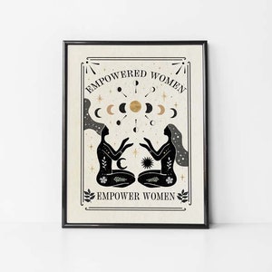 May include: Black and white illustration of two women sitting back to back with their hands raised. The women are surrounded by a circle of moons and stars. The text "EMPOWERED WOMEN EMPOWER WOMEN" is printed in black on a beige background.