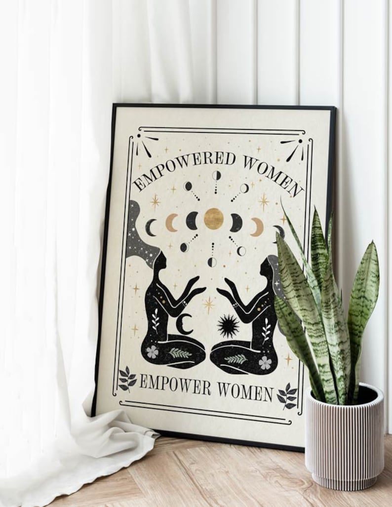 May include: A beige poster with black text that reads "Empowered Women Empower Women". The poster features a black and gold illustration of two women sitting back to back with their hands raised. The illustration is surrounded by a circle of moons and stars.