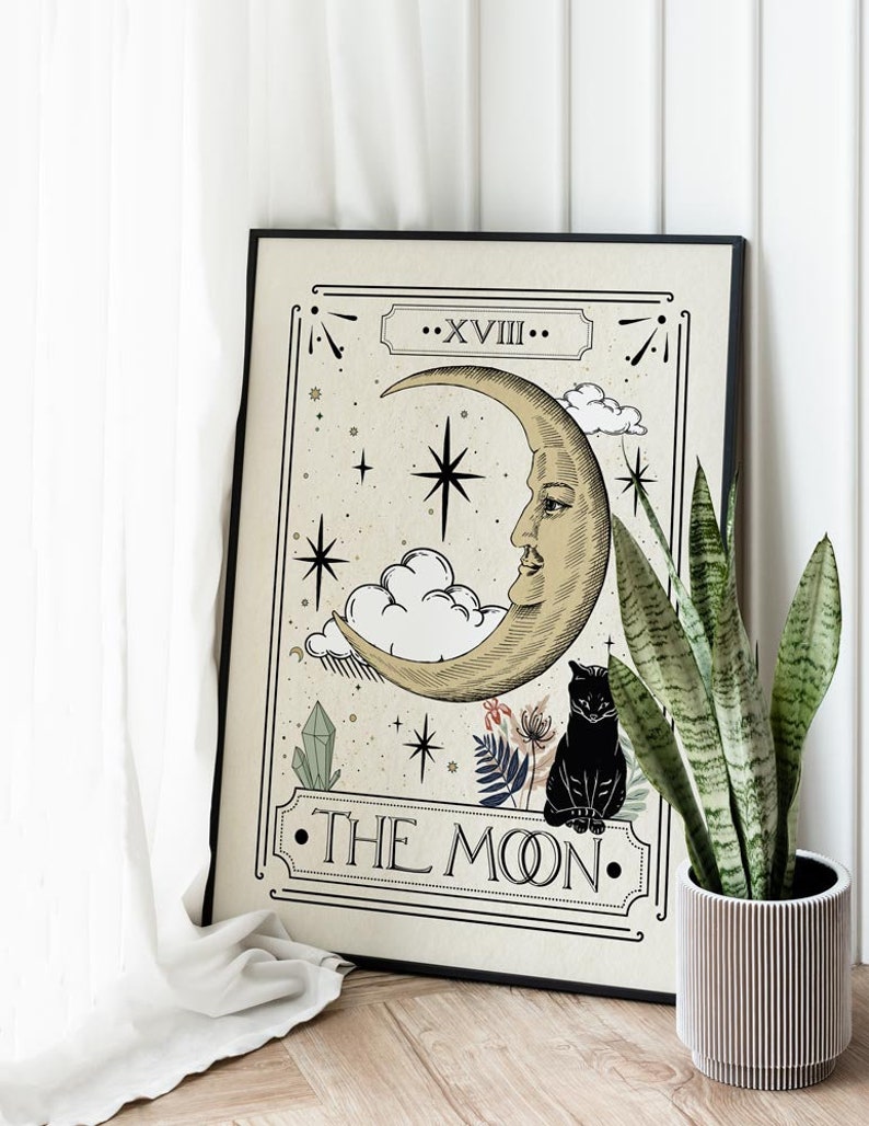K&ouml;nnte beinhalten: Ein schwarzer gerahmter Druck einer Tarotkarte, die die Mondkarte darstellt. Die Karte zeigt einen Halbmond mit einem Gesicht, eine schwarze Katze und Sterne. Der Text "XVIII. THE MOON." ist auf der Karte gedruckt.