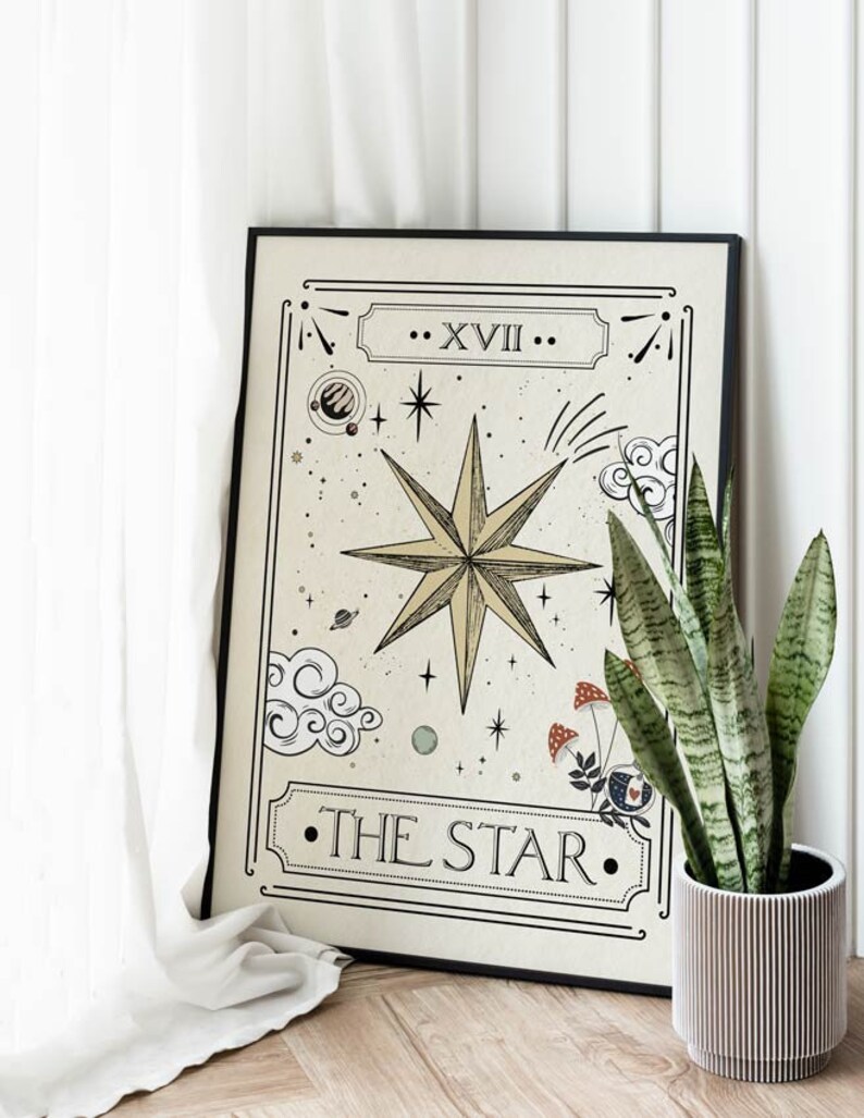 May include: A black framed print of a tarot card with a gold star and the text "...XVII... THE STAR..." on a cream background. The print is leaning against a white wall and a potted plant is in the foreground.