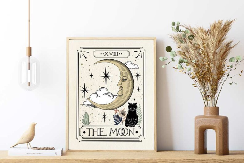 K&ouml;nnte beinhalten: Eine Tarotkarten-Illustration im Vintage-Stil mit der Mondkarte. Die Karte ist beige mit schwarzen Umrissen und zeigt einen Halbmond mit einem Gesicht, eine schwarze Katze und Sterne. Der Text auf der Karte lautet "XVIII - DER MOND".