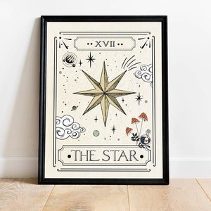 May include: A black framed print of a tarot card depicting The Star. The card features a large, eight-pointed star in gold with a white background. The card number, XVII, is written in Roman numerals at the top of the card. The text "THE STAR" is written in black at the bottom of the card.