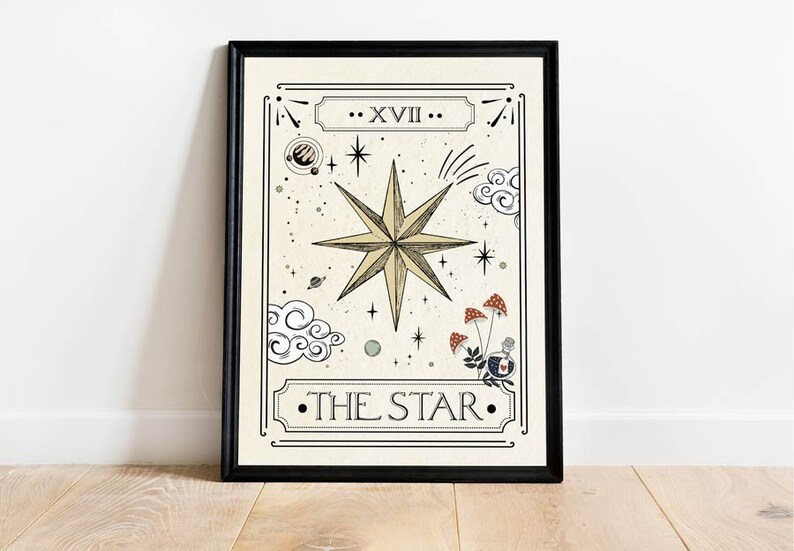 May include: A black framed print of a tarot card depicting The Star. The card features a large, eight-pointed star in gold with a white background. The card number, XVII, is written in Roman numerals at the top of the card. The text "THE STAR" is written in black at the bottom of the card.