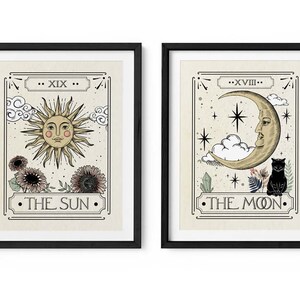 K&ouml;nnte beinhalten: Zwei gerahmte Drucke von Tarotkarten, Die Sonne und Der Mond. Die Sonnenkarte zeigt eine gelbe Sonne mit einem Gesicht und Strahlen, umgeben von Wolken und Blumen. Die Mondkarte zeigt einen zunehmenden Mond mit einem Gesicht, eine schwarze Katze und Sterne.