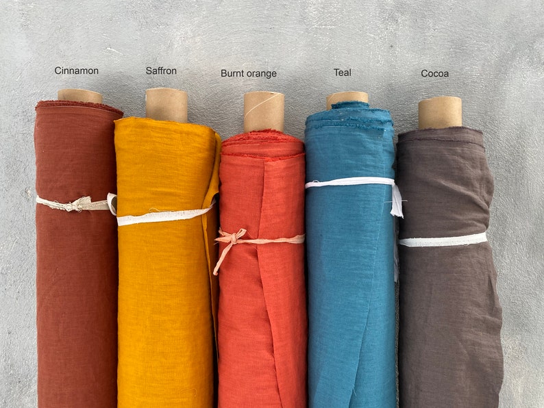 May include: Five rolls of fabric in different colors: cinnamon, saffron, burnt orange, teal, and cocoa. The fabric is rolled up and tied with a white ribbon.