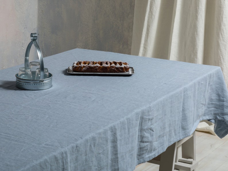 May include: A light blue linen tablecloth with a silver metal serving tray holding a baked pastry on a wooden table.