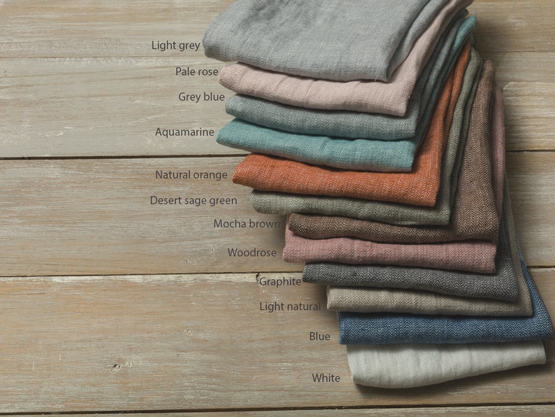 May include: A stack of 12 linen fabric swatches in various colors, including light grey, pale rose, grey blue, aquamarine, natural orange, desert sage green, mocha brown, woodrose, graphite, light natural, blue, and white.
