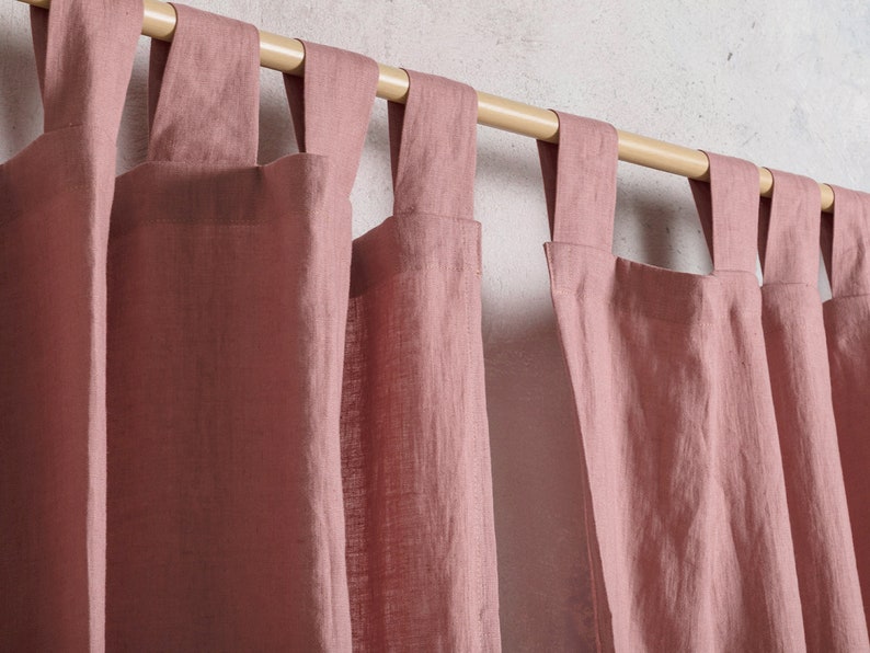 May include: Dusty rose linen curtains with a wooden rod, hanging in a window. The curtains have a simple, gathered design.