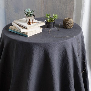 Puede incluir: Un mantel redondo de color gris oscuro con una cuerda de yute natural y dos peque&ntilde;as macetas de suculentas en una mesa con una pila de libros.