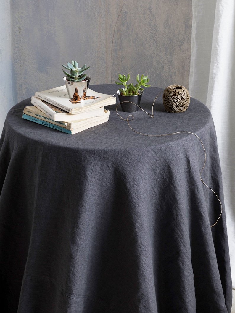 Puede incluir: Un mantel redondo de color gris oscuro con una cuerda de yute natural y dos peque&ntilde;as macetas de suculentas en una mesa con una pila de libros.