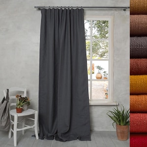 Puede incluir: Una cortina gris oscuro de cuerpo entero cuelga de una barra sobre una ventana. A la derecha, una pila vertical de muestras de tela muestra una gama de colores que incluye marrón, carbón, óxido, amarillo mostaza, naranja y rojo con textura.
