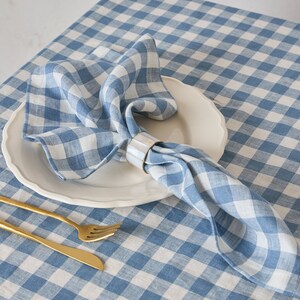 May include: A blue and white gingham tablecloth with a white plate and a blue gingham napkin with a gold napkin ring. A gold fork and knife are on the table.