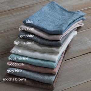 May include: A stack of ten linen napkins in various colours, including blue, pale rose, graphite, light natural, white, aquamarine, woodrose, grey blue, and mocha brown.