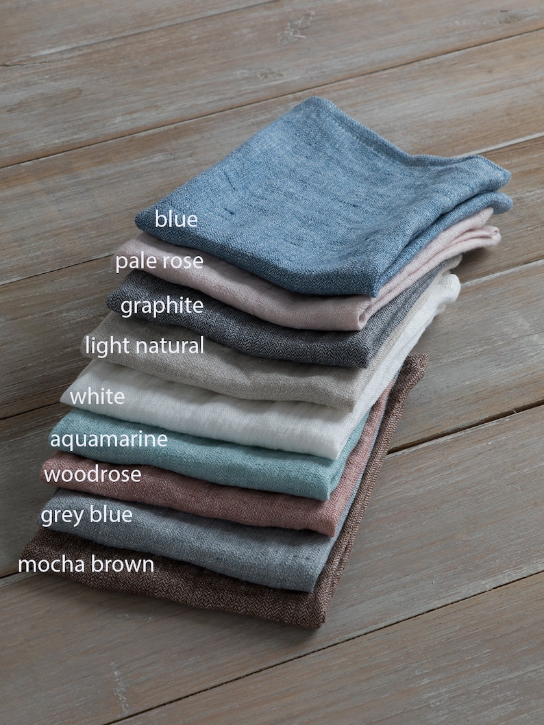 May include: A stack of ten linen napkins in various colours, including blue, pale rose, graphite, light natural, white, aquamarine, woodrose, grey blue, and mocha brown.