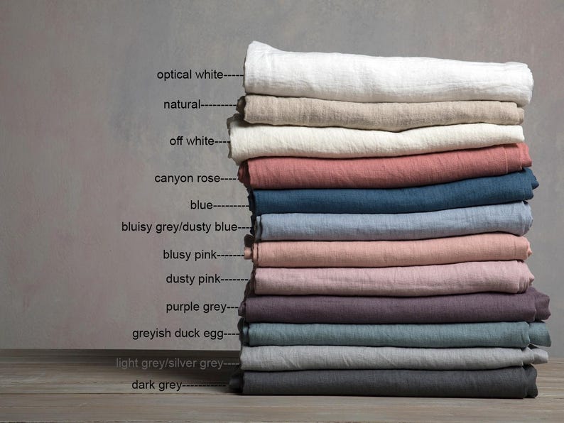 Op de afbeelding: Een stapel van 12 linnen stofstalen in verschillende kleuren, waaronder optisch wit, naturel, off white, canyon rose, blauw, stoffig blauw, stoffig roze, paars grijs, grijsachtig eendenei, licht grijs en donker grijs.
