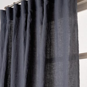 Puede incluir: Cortinas de lino gris oscuro colgadas de una barra de cortina plateada. Las cortinas están hechas de una tela suave y texturizada.