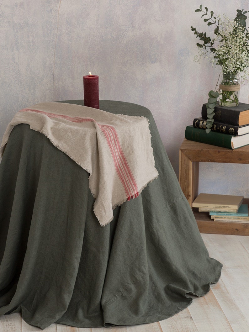 Puede incluir: Un mantel de lino verde con una servilleta de lino a rayas rojas y blancas sobre una mesa redonda. Una vela roja est&aacute; sobre la mesa.