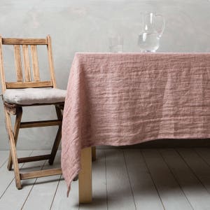 May include: A pink linen tablecloth draped over a wooden table with a wooden chair and two glasses and a pitcher of water on top.