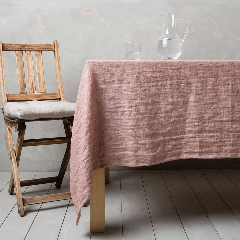 May include: A pink linen tablecloth draped over a wooden table with a wooden chair and two glasses and a pitcher of water on top.