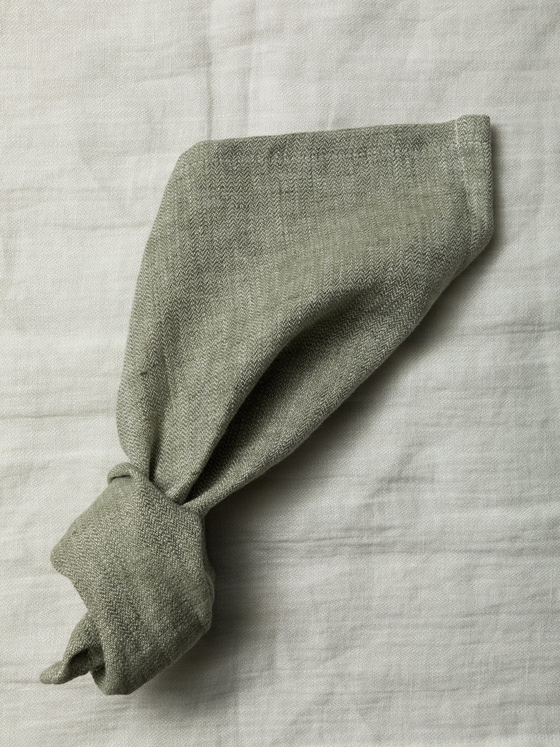 May include: A green linen napkin with a herringbone pattern, folded and tied into a knot.