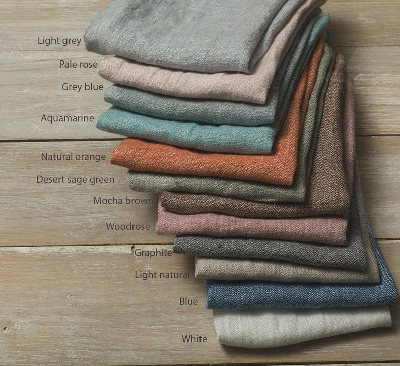 May include: A stack of 12 linen fabric swatches in various colors, including light grey, pale rose, grey blue, aquamarine, natural orange, desert sage green, mocha brown, woodrose, graphite, light natural, blue, and white.