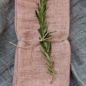 May include: A pink linen napkin folded in half and tied with twine, with a sprig of rosemary on top.
