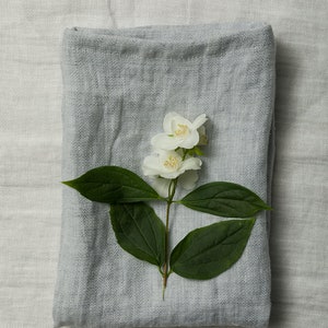 May include: A gray linen throw blanket with a sprig of white jasmine flowers on top.