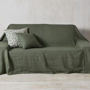 Op de afbeelding: Een groene linnen sofa deken met twee kussens, een met een bloemenpatroon en een effen groen.