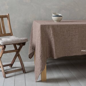 May include: A mocha brown linen tablecloth with a wooden table and a wooden folding chair with a light beige cushion. The tablecloth has a subtle texture and is draped over the table.