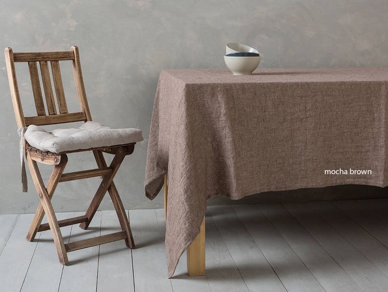 May include: A mocha brown linen tablecloth with a wooden table and a wooden folding chair with a light beige cushion. The tablecloth has a subtle texture and is draped over the table.